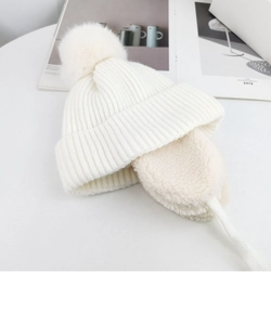 Close-up of cream white knit earflap hat with soft pompom for kids on a minimalist background