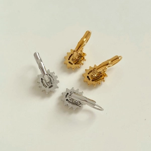 Détail de boucles d'oreilles fleur dorées et argentées avec design de pétales en engrenage