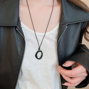 Détail du collier à pendentif ovale noir irrégulier sur cordon noir au style minimaliste