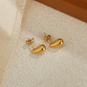 Polished gold bean-shaped stainless steel earrings on a minimalist textured surface