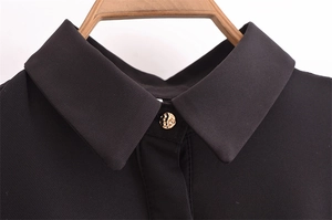 Close-up of black long sleeve dress neckline with a textured gold hammered button detail