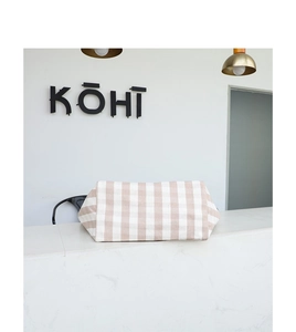 Detail of beige and white checkered canvas handbag placed on a minimalist white counter