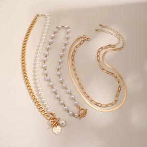 Detail of layered gold link necklaces with pearls and coin pendant on beige background