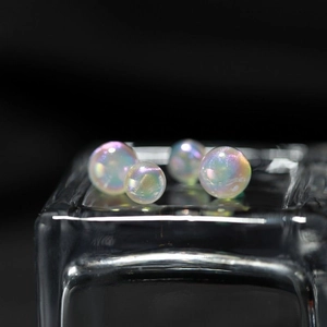 Iridescent mermaid pearl stud earrings with rainbow luster on a dark glass base