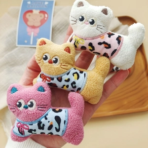 Close-up of three cute plush cat dolls in colorful leopard print outfits on a hand