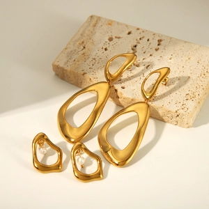 Irregular golden geometric drop earrings with pearls on decorative stone background
