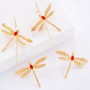 Détail de boucles d'oreilles libellule dorées avec cristaux rouges et ailes gravées