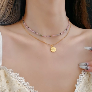 Détail d'un collier de perles superposé avec pendentif soleil sur chaîne dorée