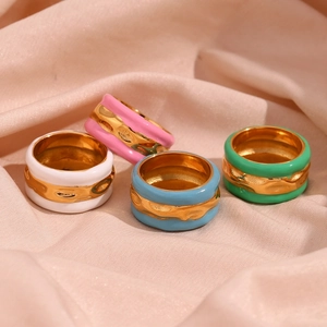 Detail of colorful enamel and golden water wave rings on soft pink silk fabric