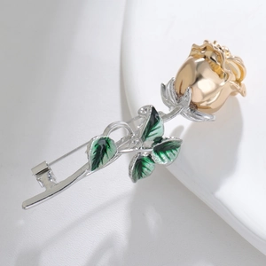 Detailed close-up of a gold-plated rose brooch with green enamel leaves on white ceramic