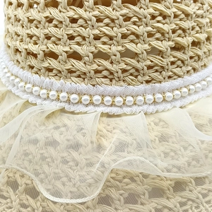 Close-up of woven straw sun hat with delicate white lace, pearls and organza details