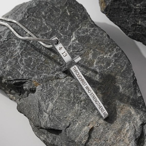Détail du pendentif en croix avec texte biblique gravé sur une roche texturée