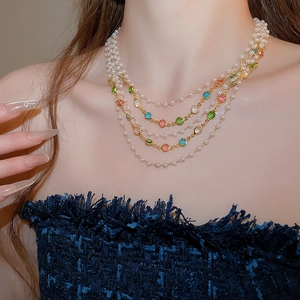 Detail of layered gold necklace with colorful gemstones and pearls worn on collarbone