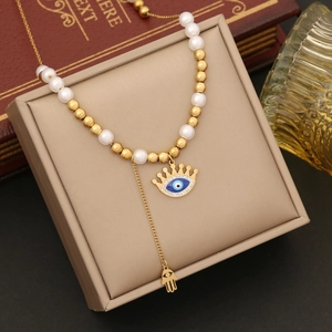 Detail of gold evil eye and hamsa hand pendant on pearl bead necklace over jewelry box
