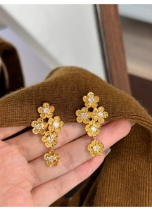 Detail of gold flower earrings with five petals and zircon centers in brushed metal finish