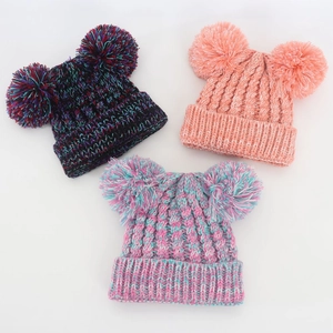 Close-up of knit winter baby hats with double pompoms in mixed colors and ribbed cuffs