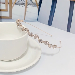 Elegant gold wavy headband with clear rhinestones placed on a white ceramic teacup