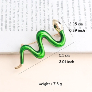 Macro shot of green enamel snake brooch with gold accents and sparkling gemstone eyes
