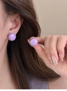 Détail de boucle d'oreille bouton ronde violette brillante portée, montrant l'éclat poli