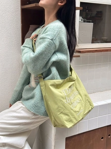 Detail of light green canvas tote bag with embroidered text and shoulder strap