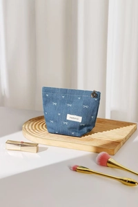 Close-up of denim cosmetic bag with white bow pattern and golden petal zipper pull