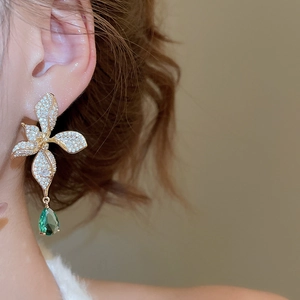 Macro view of luxurious gold-plated flower earrings with sparkling green teardrop pendants