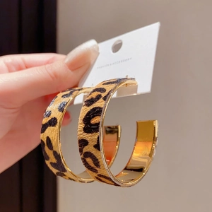 Leopard print C-shaped hoop earrings with gold metal interior in a handheld close-up view