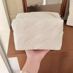 Close-up of white shell-quilted cosmetic bag with gold zipper and portable nylon texture