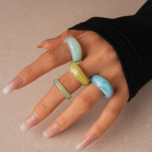 Close-up of chunky colorful acrylic resin rings worn by a model on a stone background