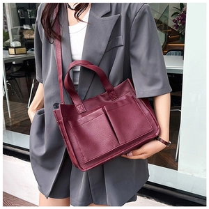 Detail of dark burgundy leather tote bag with front pockets on a grey suit model