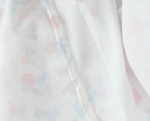 Close-up of white fabric with pink and blue floral embroidery and detailed stitching