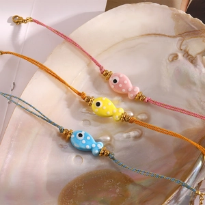 Three-piece set of fish charm woven bracelets in pink, yellow, and blue on a shell tray