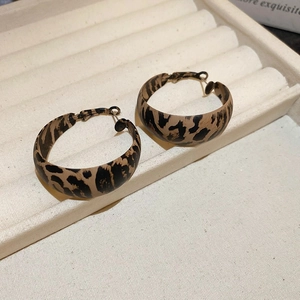 Macro detail of retro leopard print hoop earrings on a beige wavy jewelry display