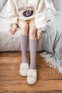 Detail of purple coral fleece knee-high socks paired with cozy off-white plush slippers