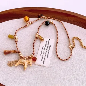 Ethnic woven rope necklace with golden horse pendant and beaded tassels on rustic linen