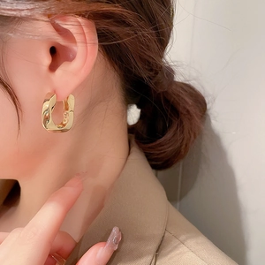 Gros plan d'un mannequin portant une boucle d'oreille en U géométrique dorée et torsadée
