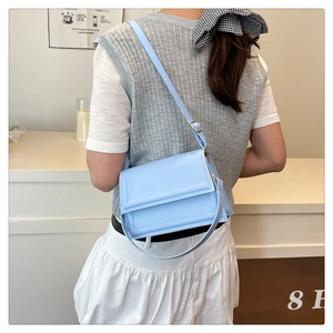 Blue PU leather crossbody bag worn by model featuring an adjustable strap and flap cover