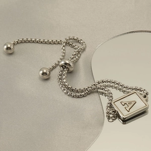 Detail of adjustable stainless steel bracelet with letter A square pendant on silver fabric