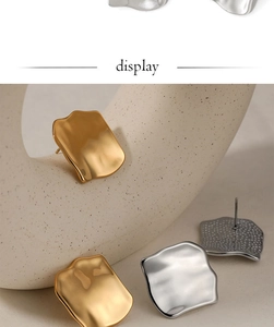 Detail showing irregular gold and silver square earrings with ripple texture on white stand