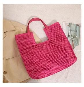 Flat lay of pink woven straw tote bag on textured cloth with beige trench coat