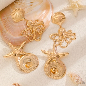 Macro shot of gold octopus and starfish earrings on white sand with sea shells