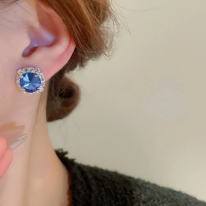 Nahaufnahme von blauen runden Kristallohrringen mit Diamantumrandung am Modell