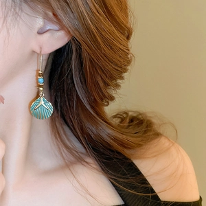Detail of bohemian starfish shell earrings worn on model featuring teal enamel and gold finish
