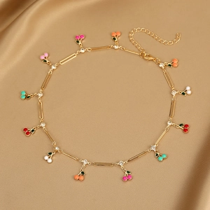 Detail shot of golden cherry pendant necklace with colorful enamel on champagne satin