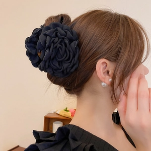 Detail of a large black fabric rose hair claw clip shown on a woman elegant bun