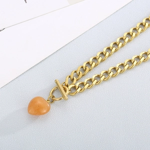 Detailed shot of golden chain bracelet featuring an orange heart pendant and OT buckle