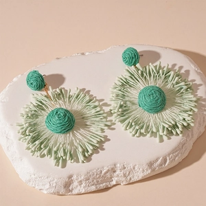 Detailed view of handmade woven floral earrings with green and white raffia tassels
