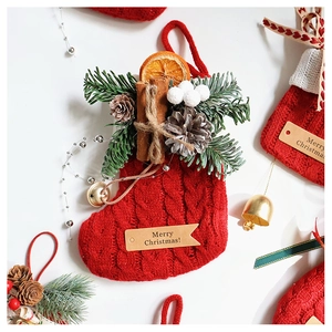 Close-up of red knit Christmas stocking with pine cones, cinnamon, and golden bell details