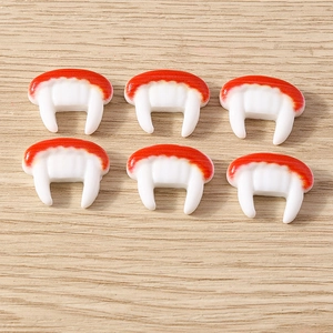 Detailed view of red and white resin vampire fang charms for Halloween DIY crafts and decor