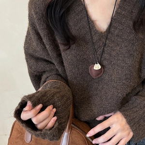 Detail of a brown leather heart pendant with Take It Easy engraving on a knitted sweater